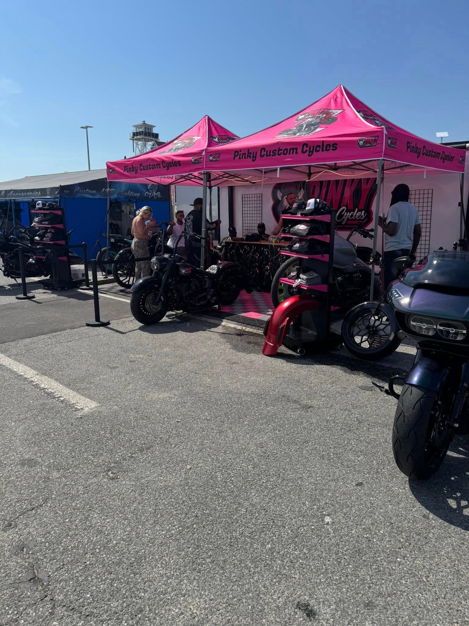 Pink-canopied vendor booth at an outdoor motorcycle event, selling parts.