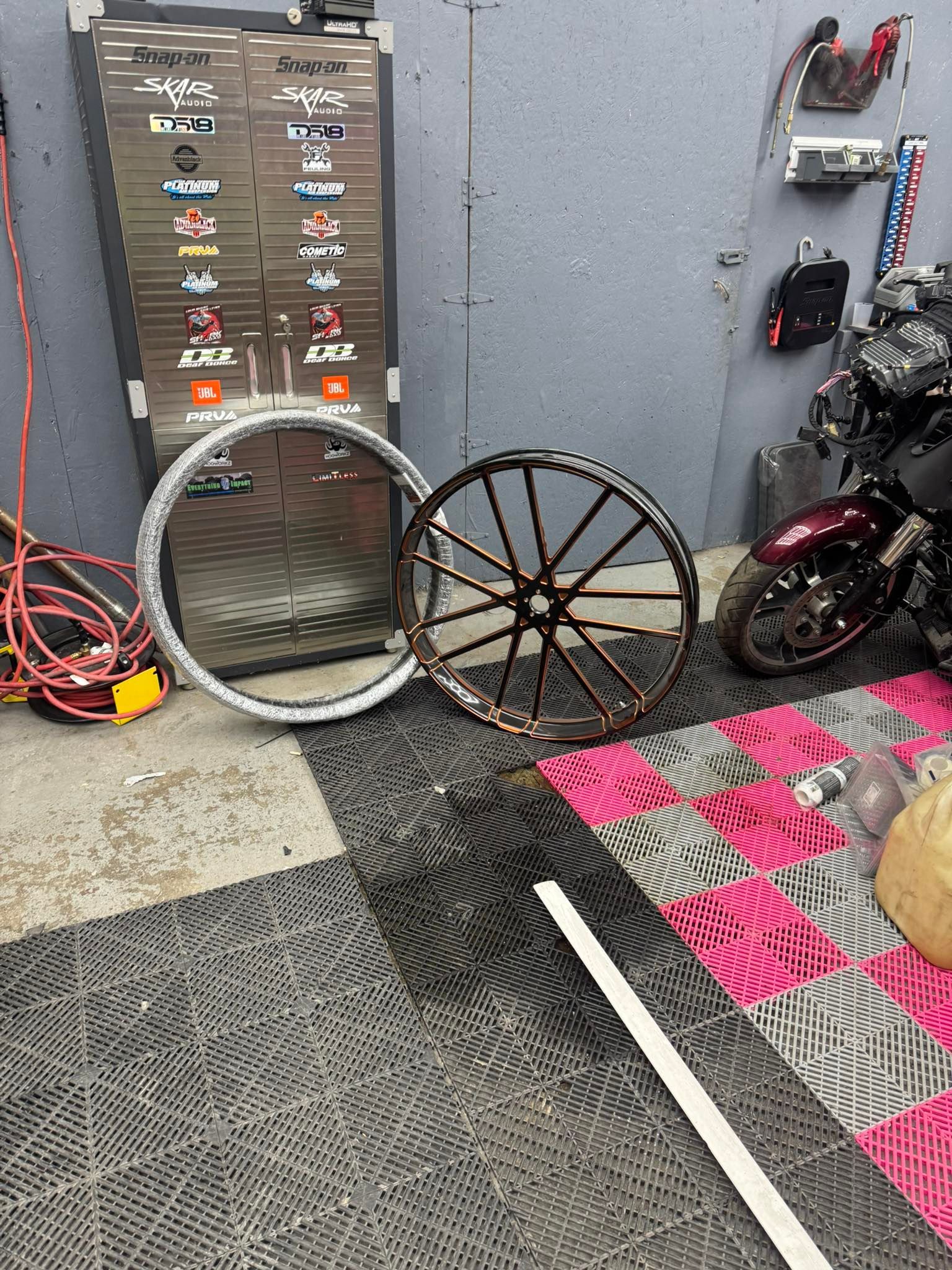Two motorcycle wheels on the floor with equipment, a motorcycle, and a cabinet in a garage.