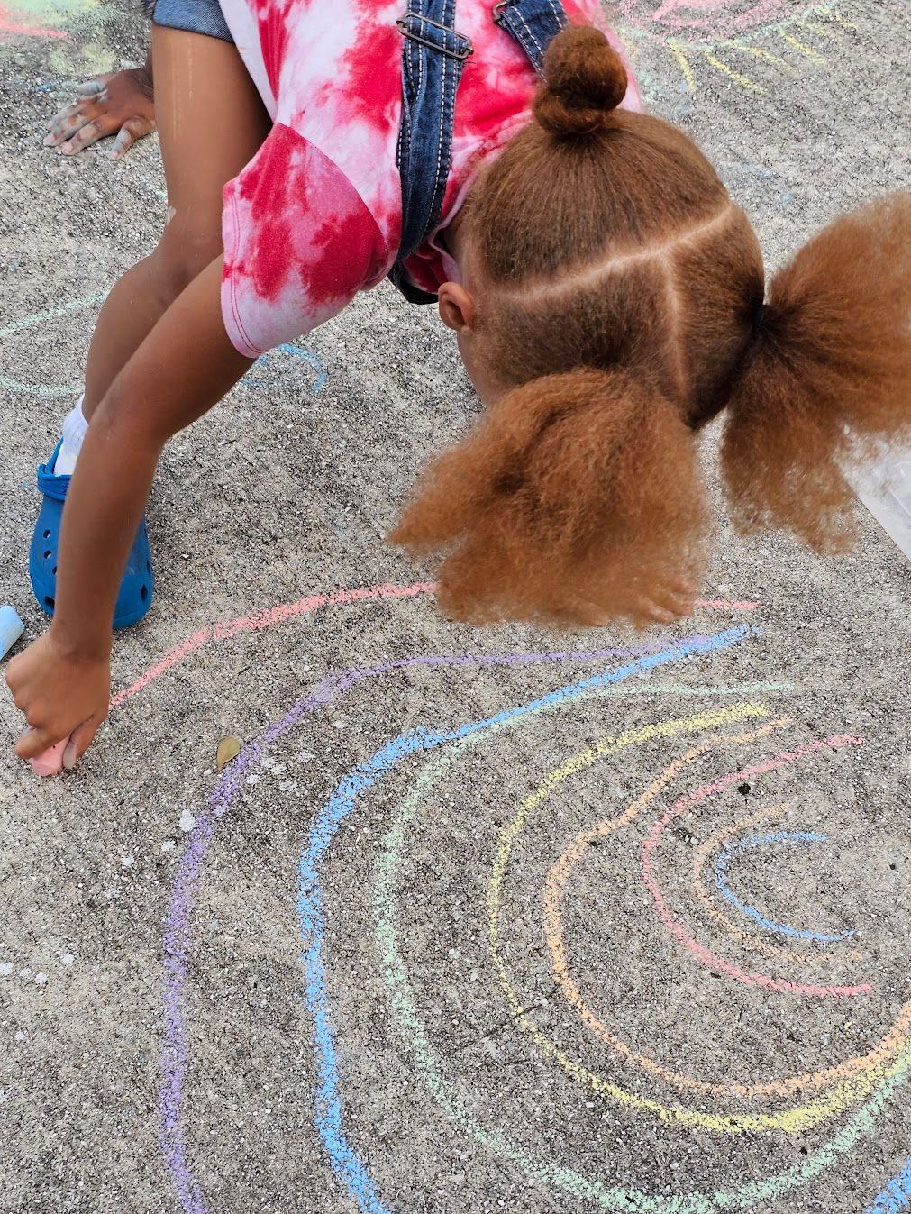A little girl is drawing with chalk on the ground