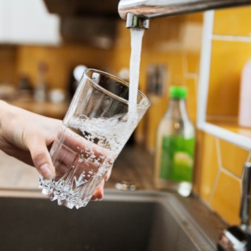A person is pouring water into a glass from a faucet.