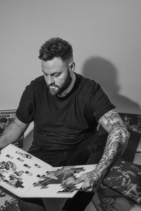 A man with tattoos is sitting on a couch reading a book.