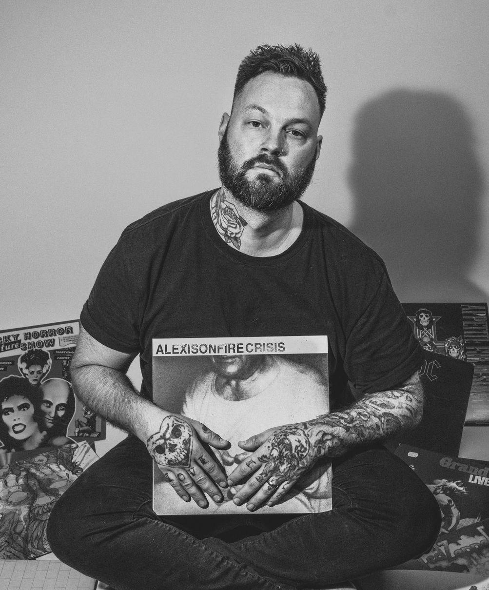 A man with a beard and tattoos is sitting on the floor holding a record.