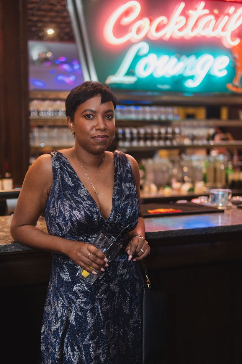 A woman in a blue dress is standing in front of a neon sign that says cocktail lounge.