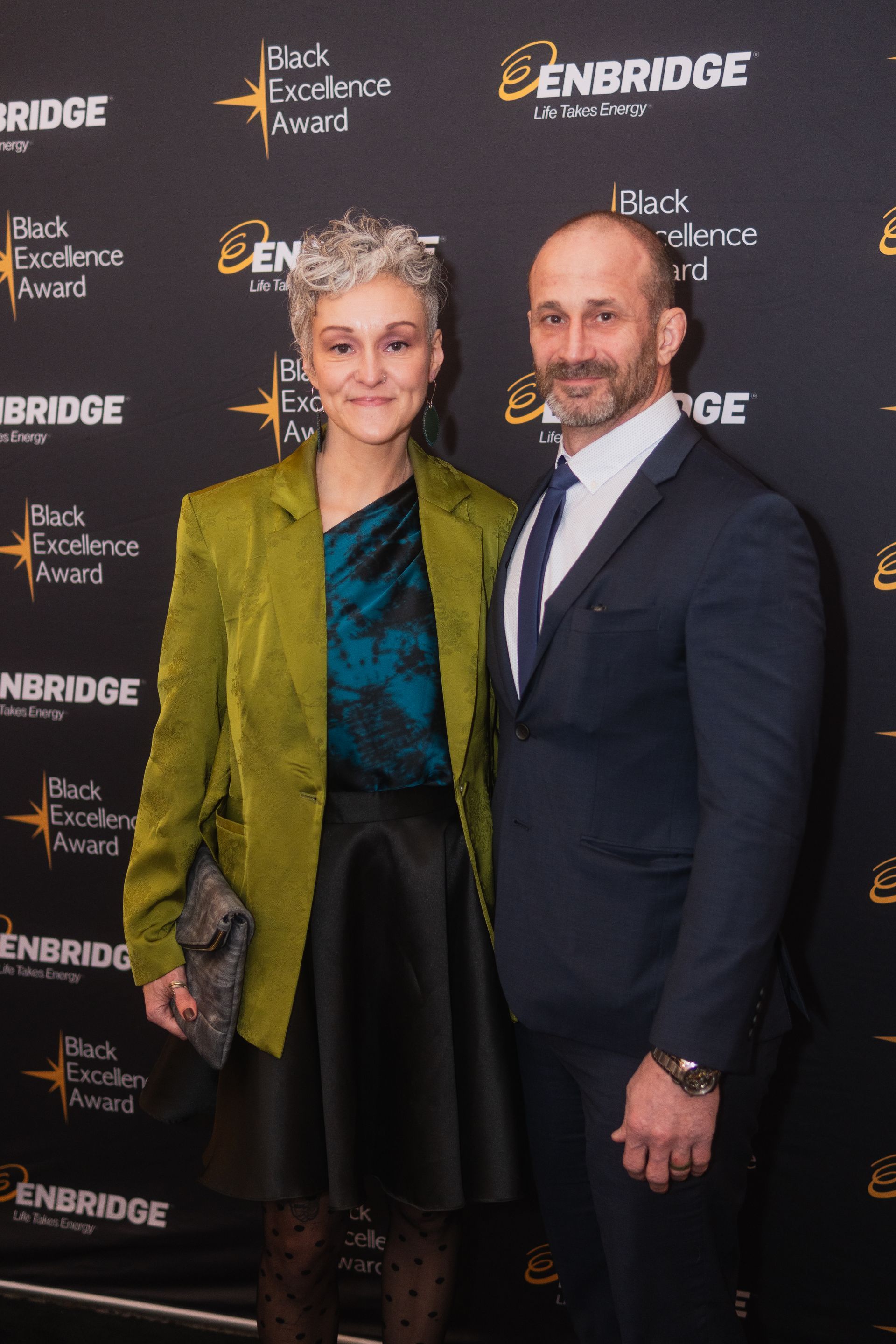 A man and a woman are posing for a picture on a red carpet.