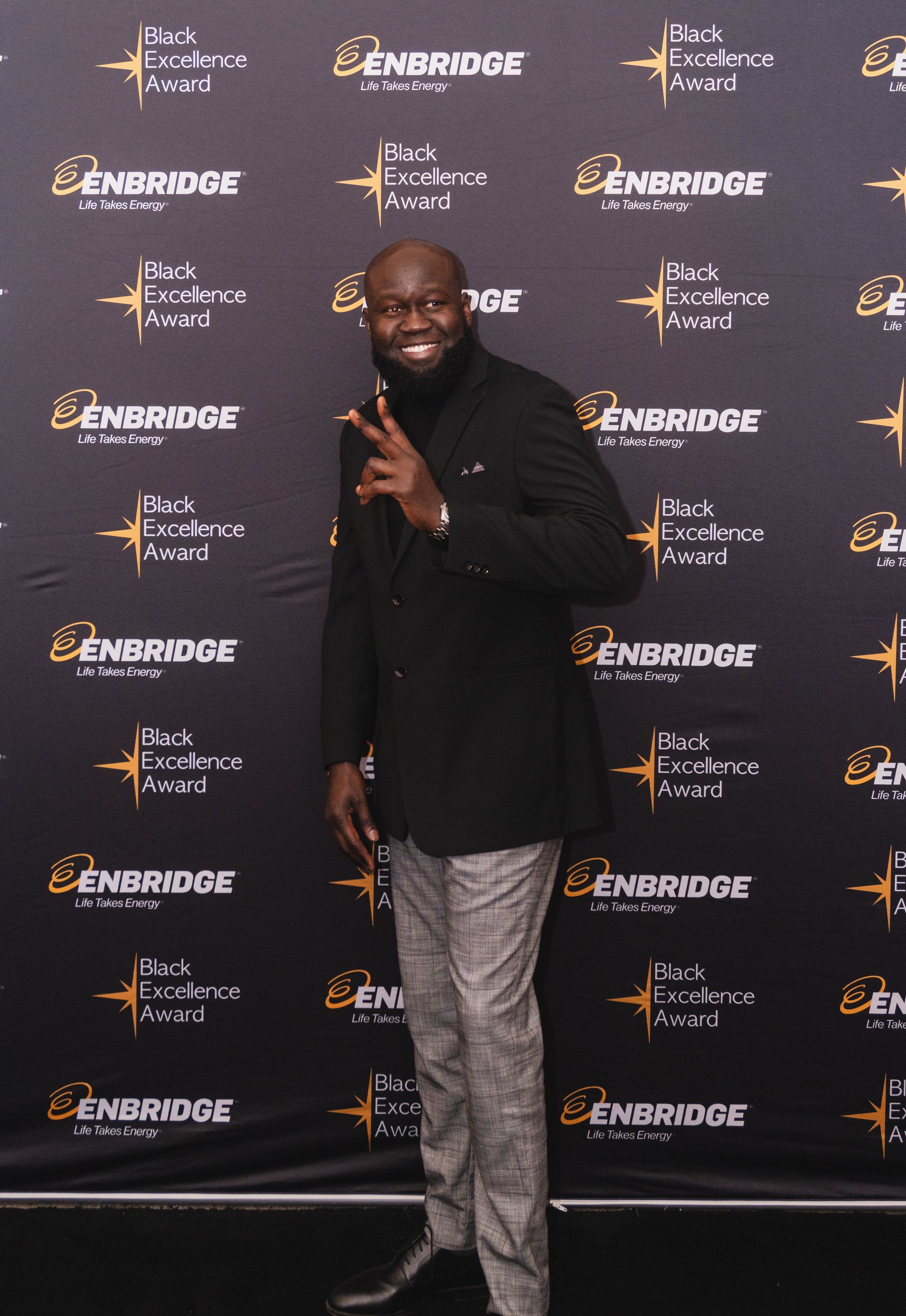 A man in a black suit is standing in front of a black backdrop that says benbridge