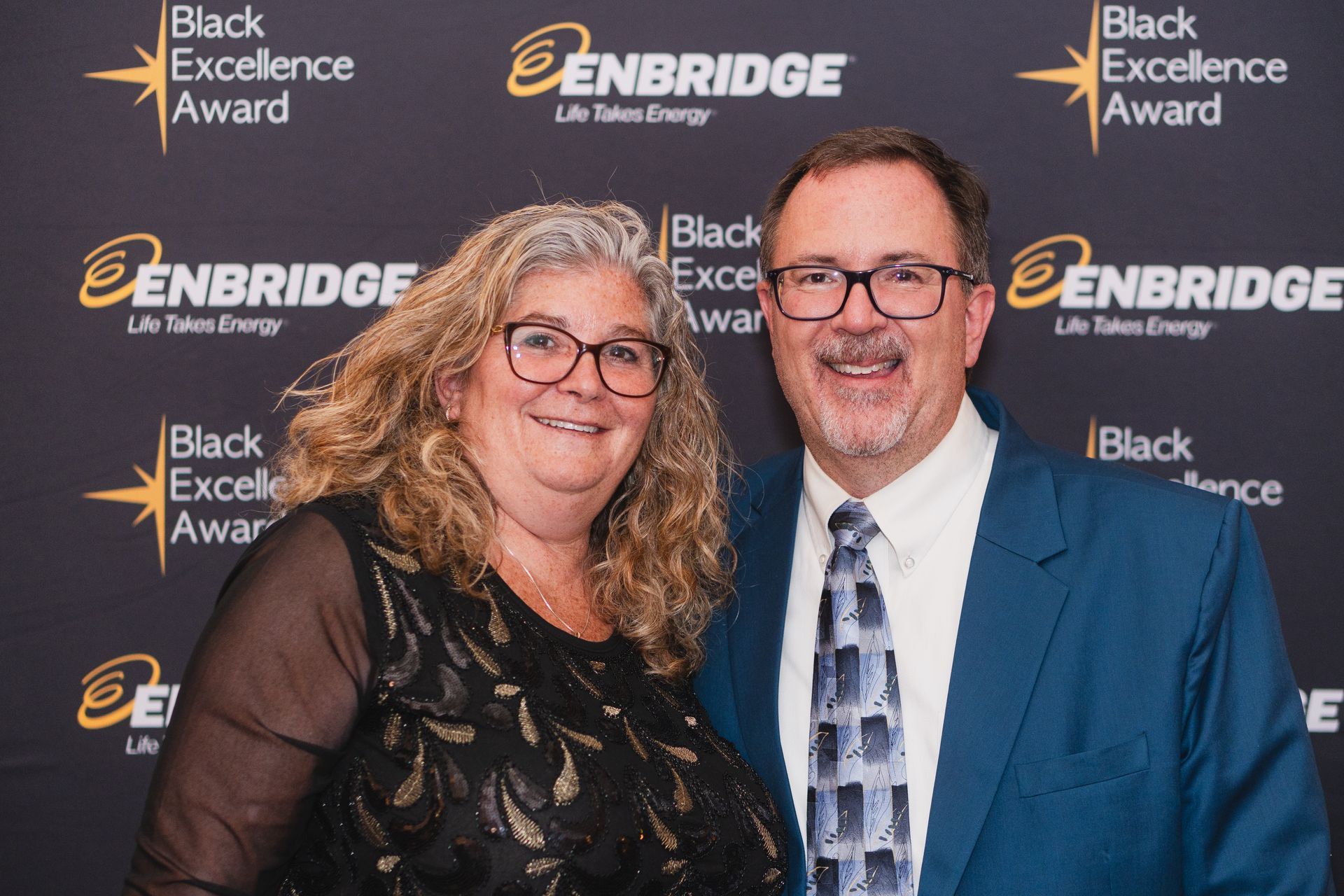 A man and a woman are posing for a picture in front of a black background.