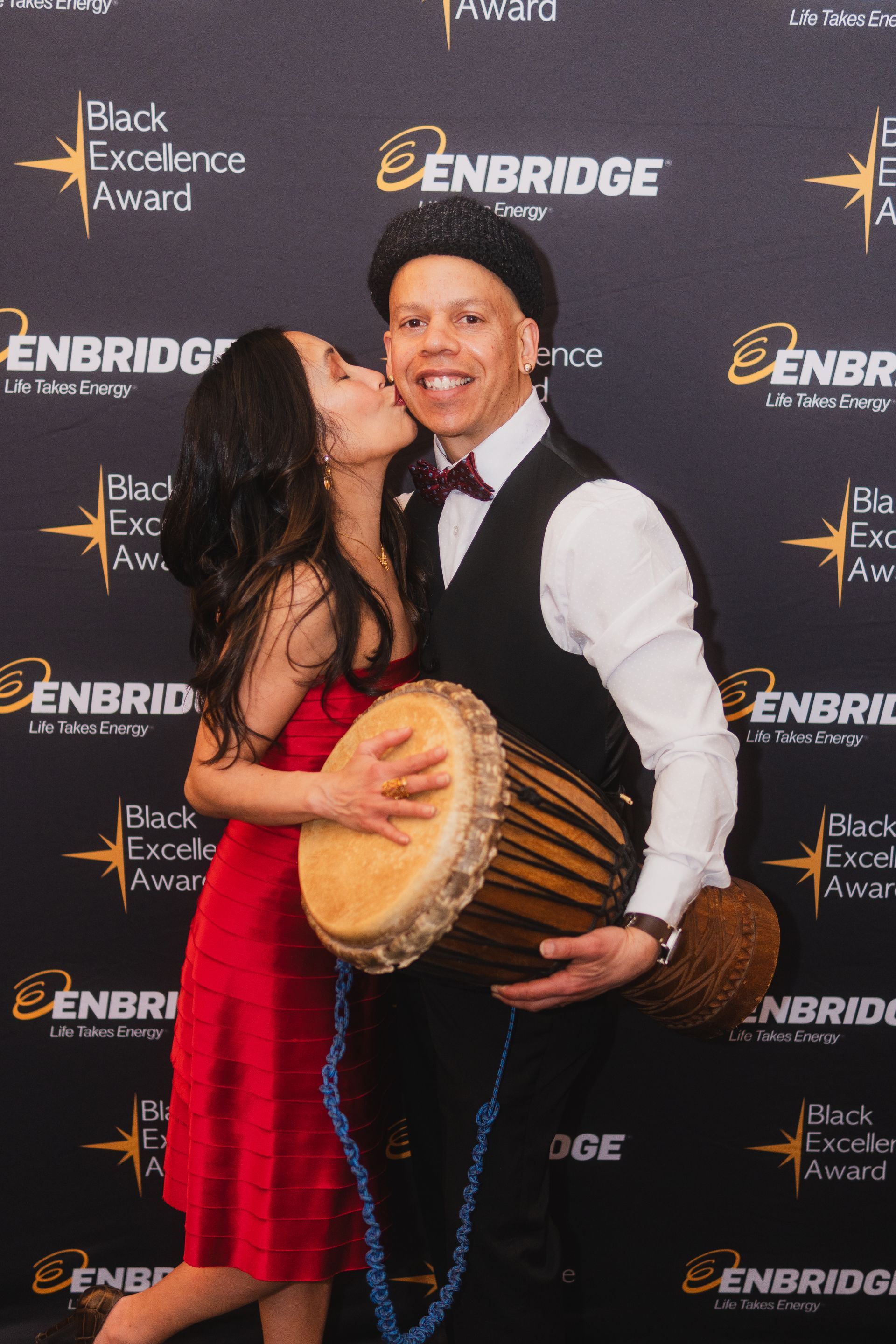 A man and a woman are kissing while holding a drum.