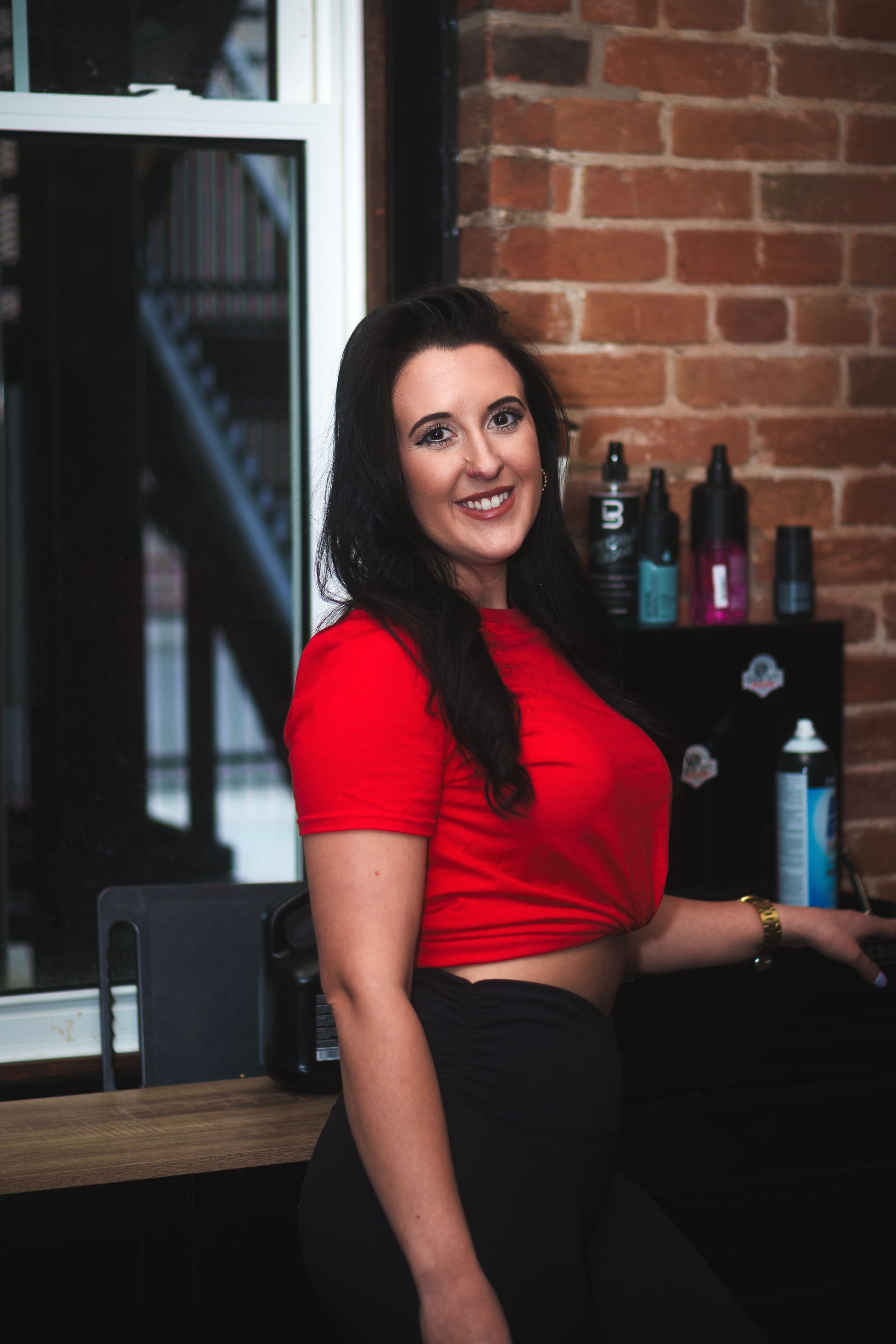 A woman in a red crop top is standing in front of a brick wall.