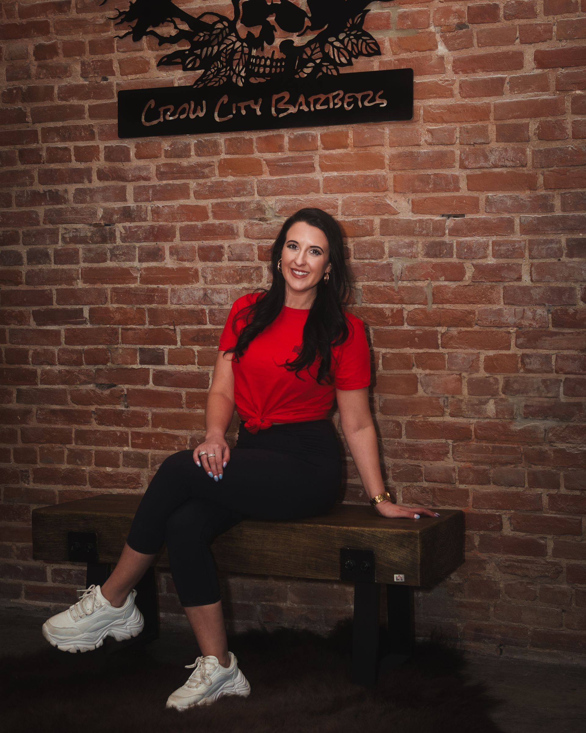 A woman is sitting on a bench in front of a brick wall.