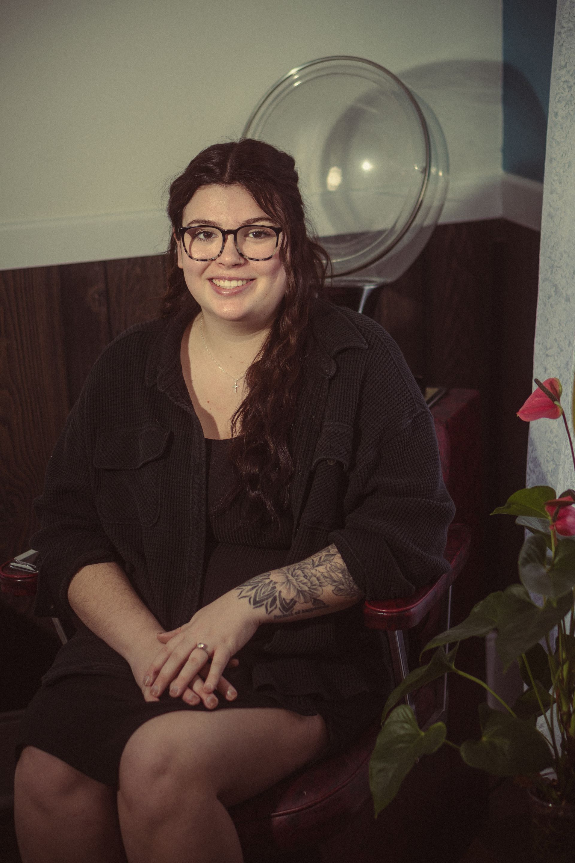 A woman wearing glasses and a black dress is sitting in a chair.