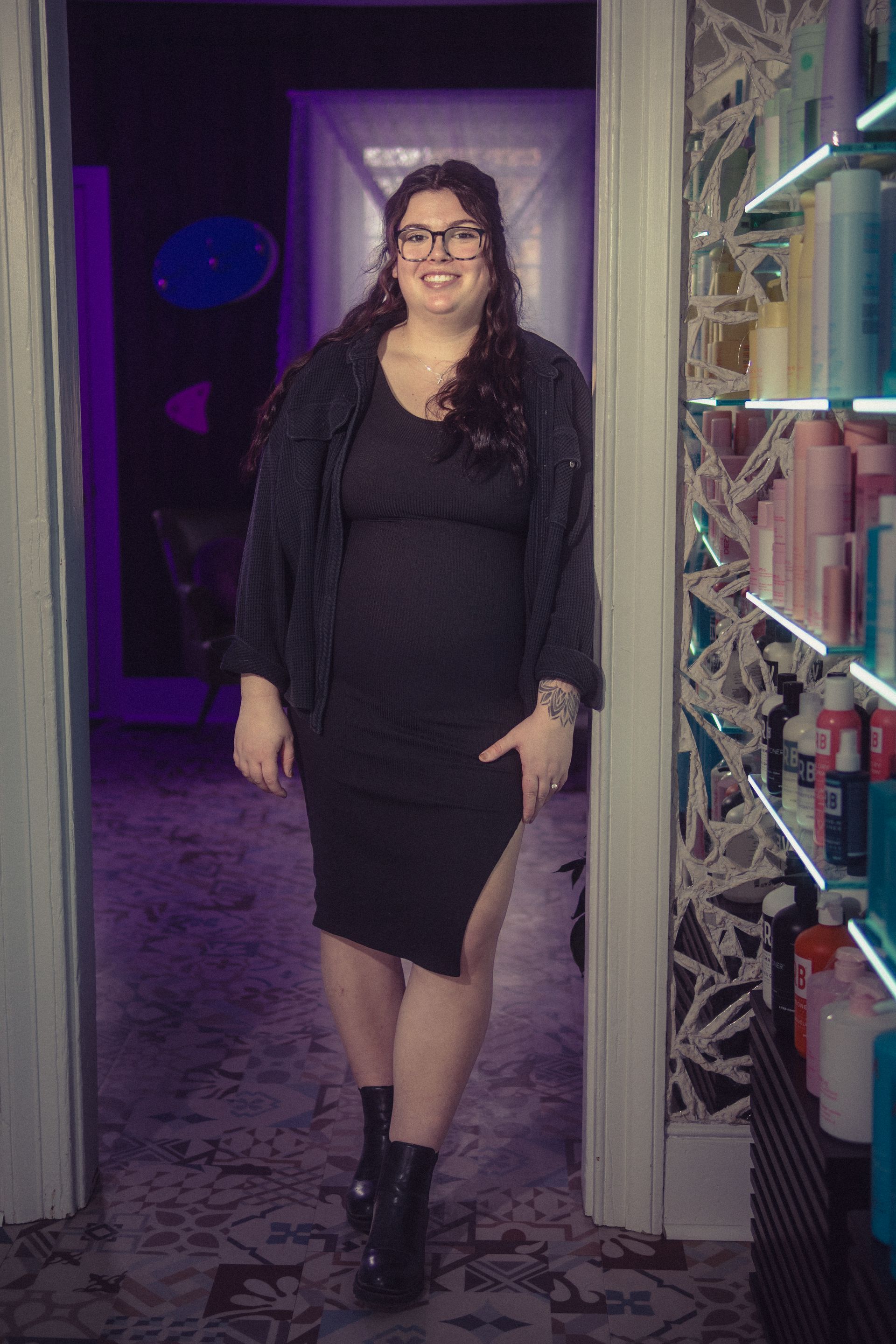 A woman in a black dress and glasses is standing in a doorway.
