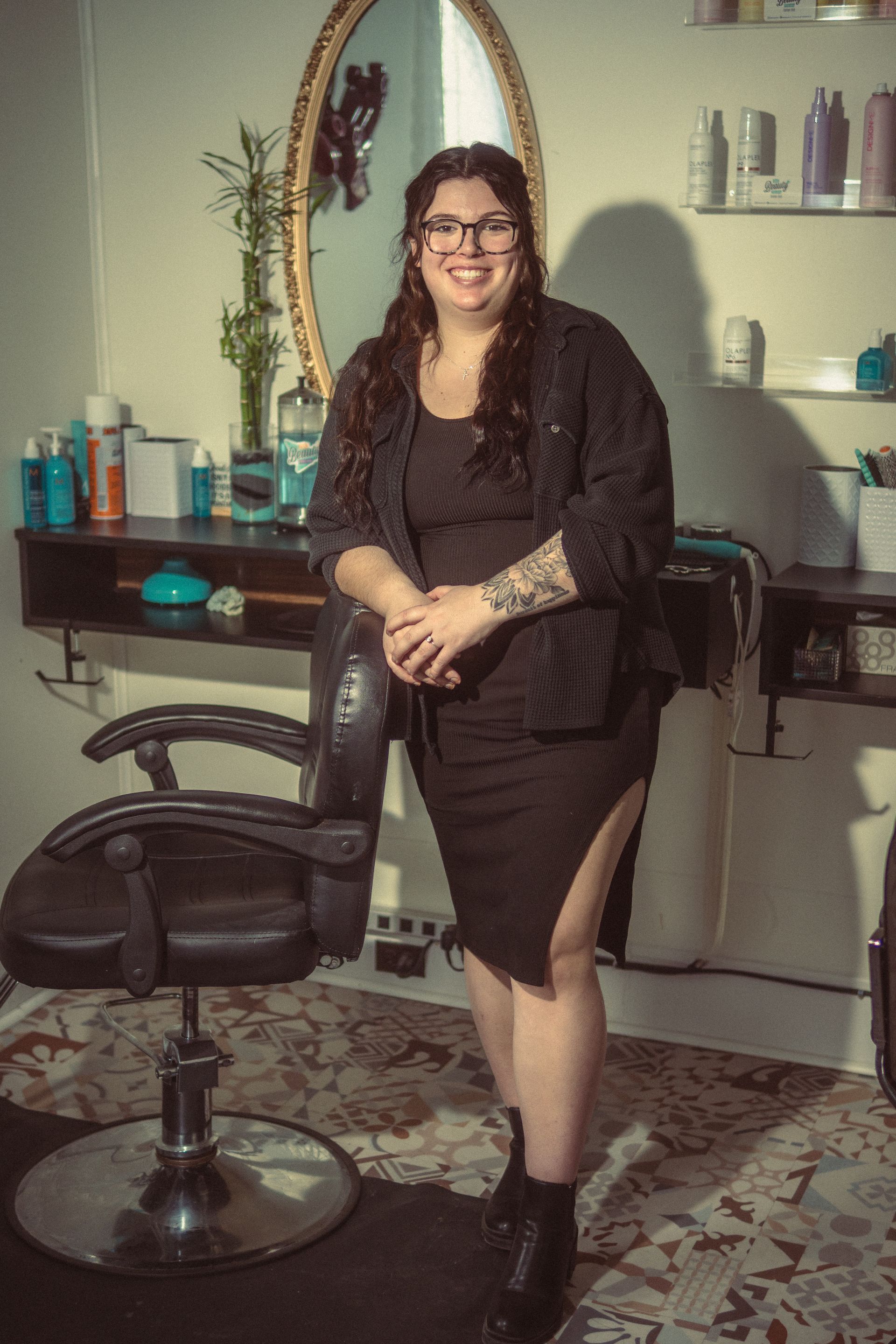 A woman in a black dress is standing in front of a hair salon chair.