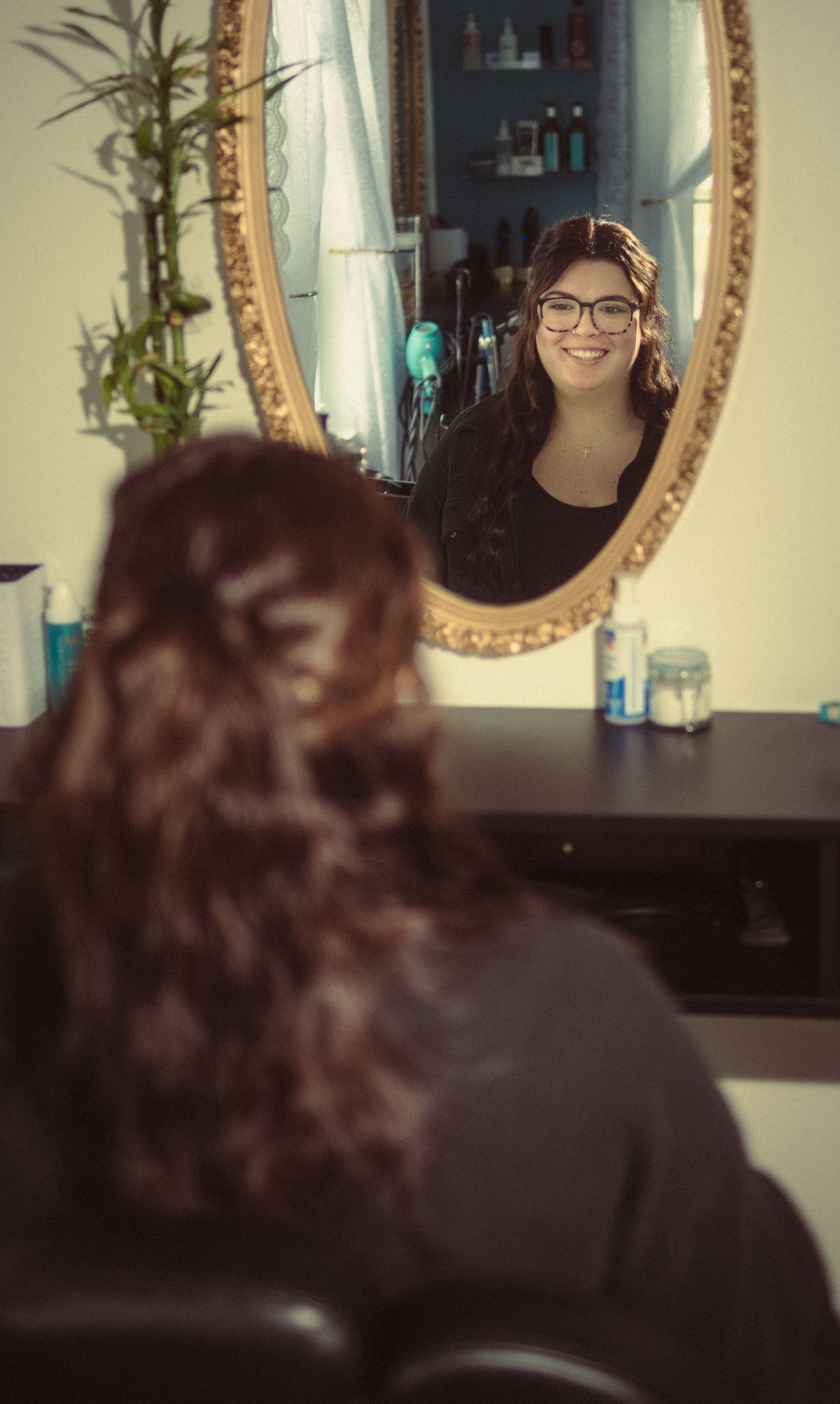 A woman is sitting in front of a mirror looking at herself.