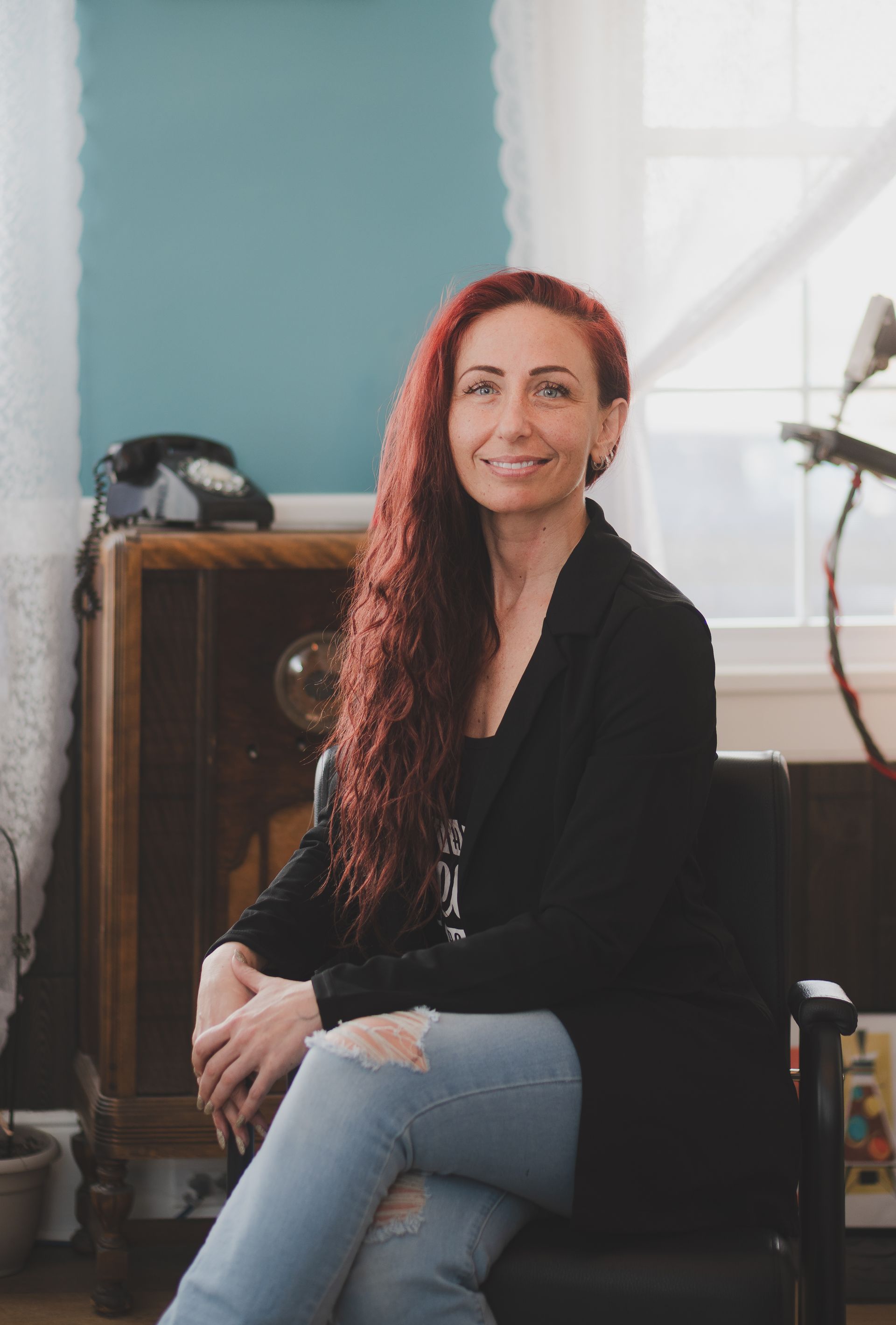 A woman with red hair is sitting in a chair in front of a window.
