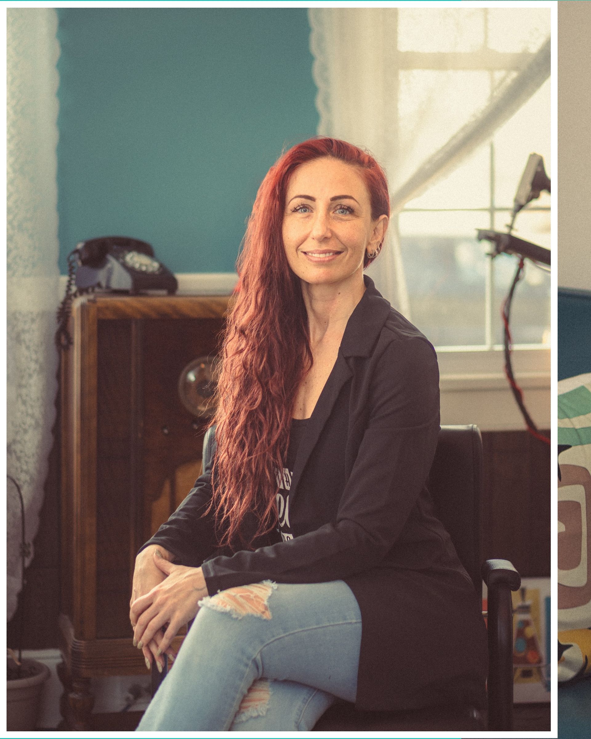 A woman with red hair is sitting in a chair in front of a window.
