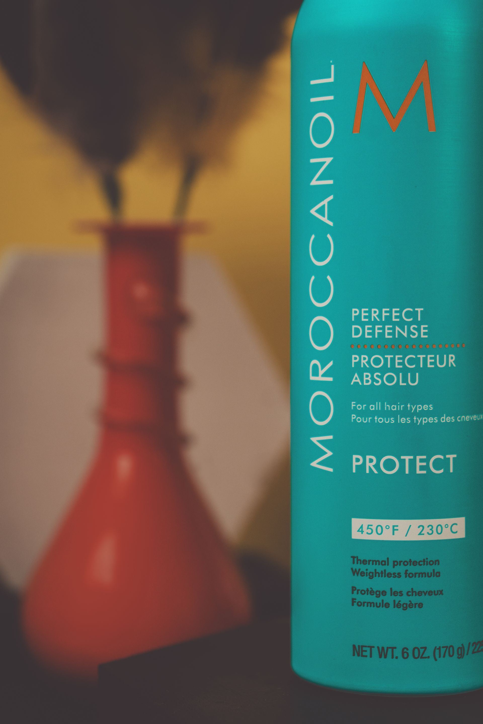 A bottle of moroccanoil perfect defense shampoo is sitting next to a vase.