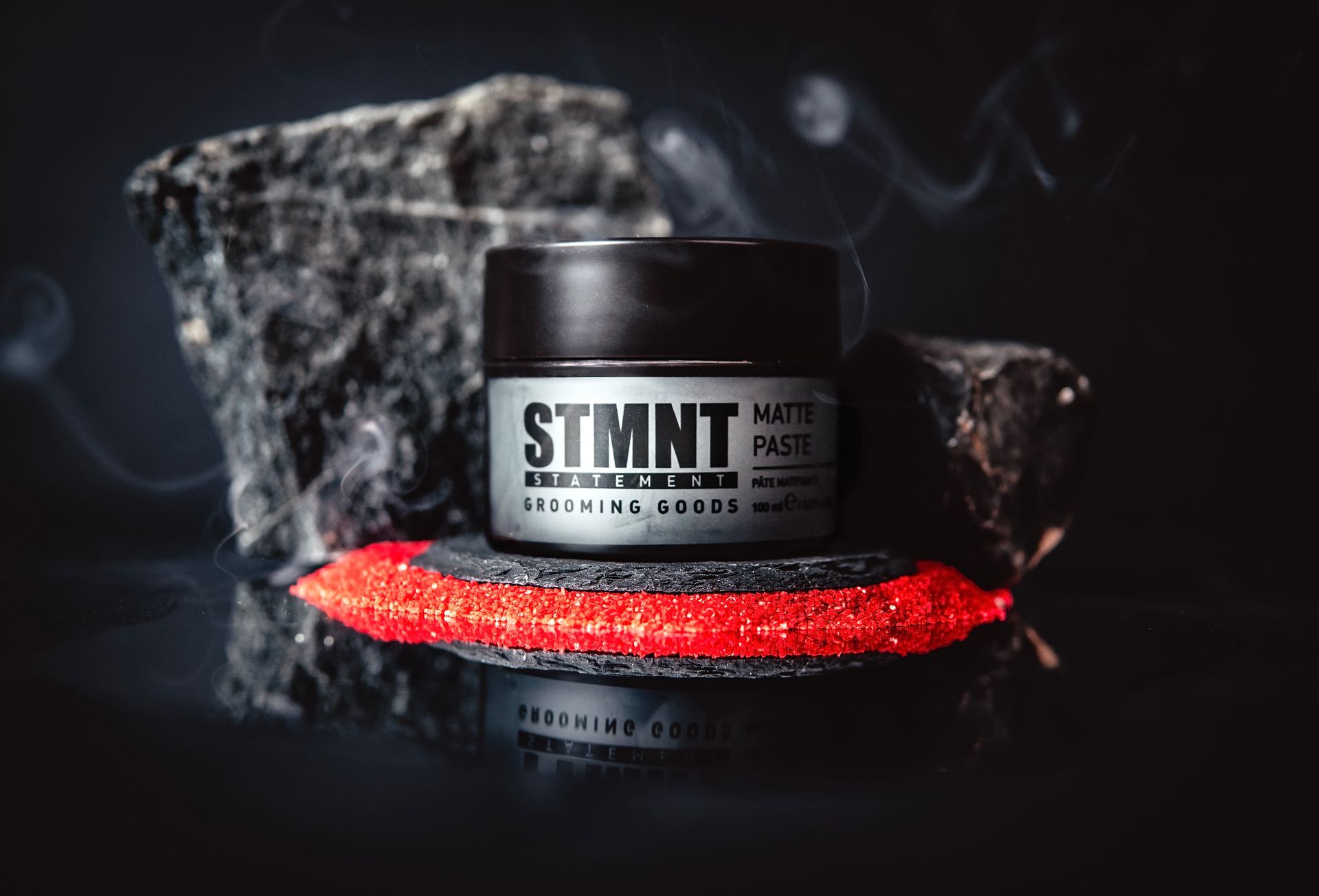 A jar of stmnt matte paste is sitting on a rock.
