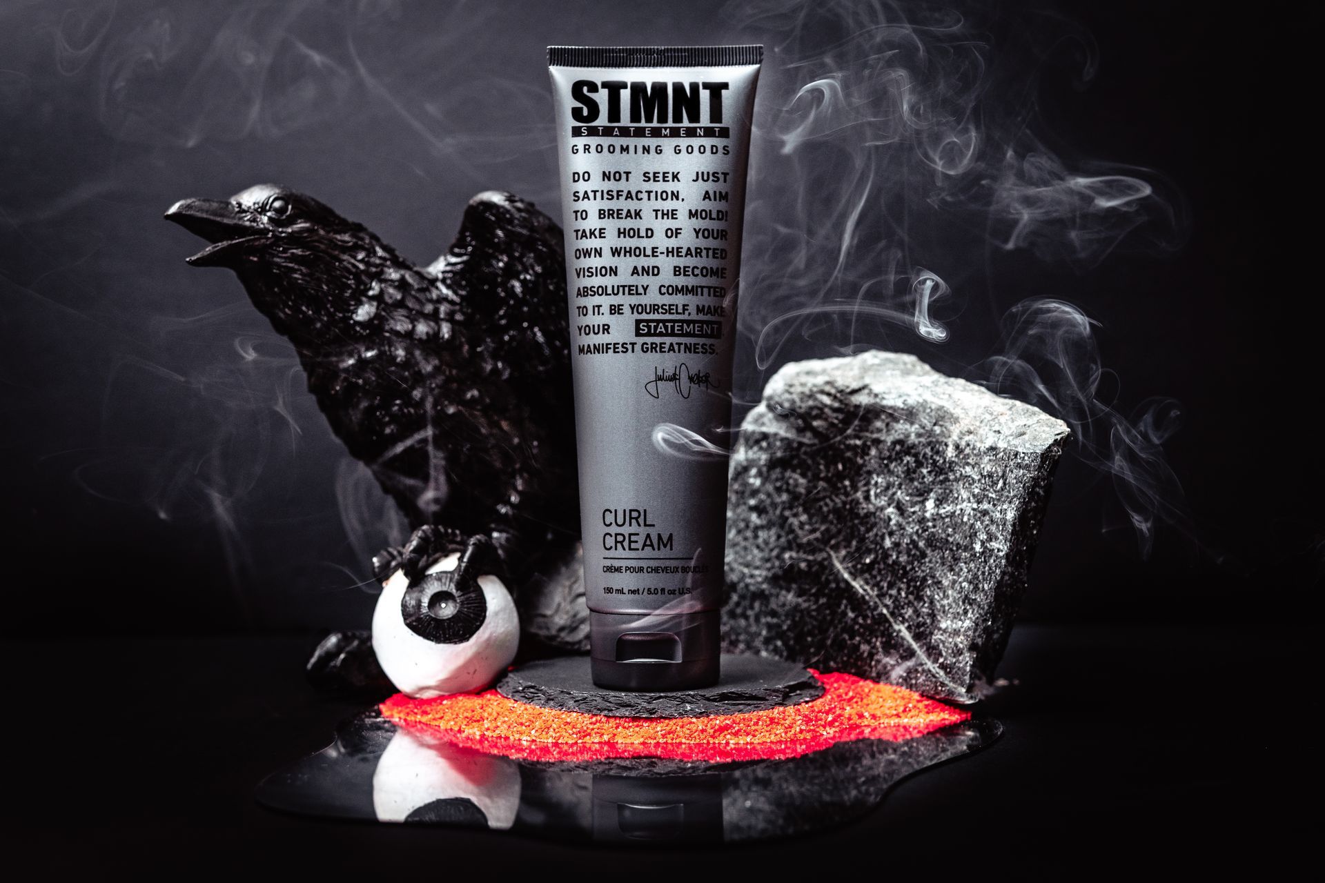 A tube of stmnt lotion is sitting on a rock next to a statue of a crow.
