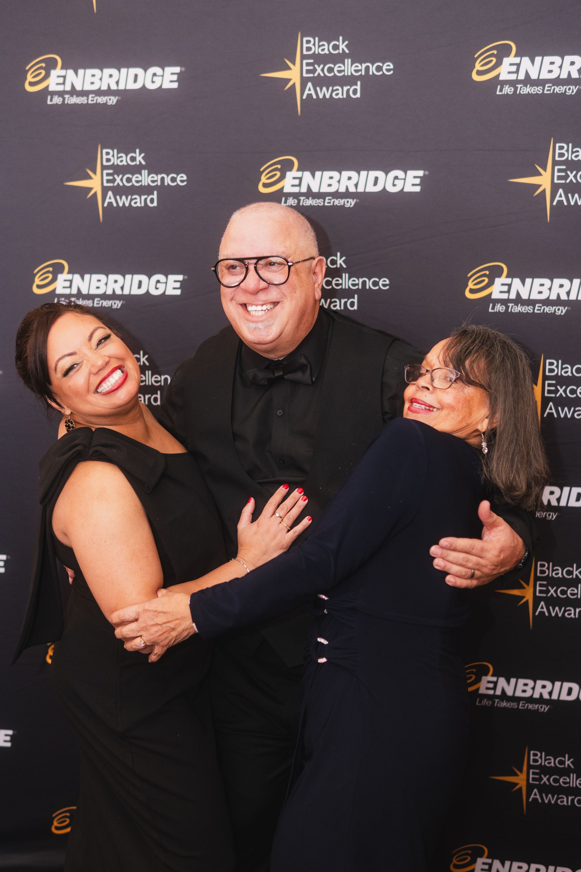 A man and two women are hugging each other in front of a black background.