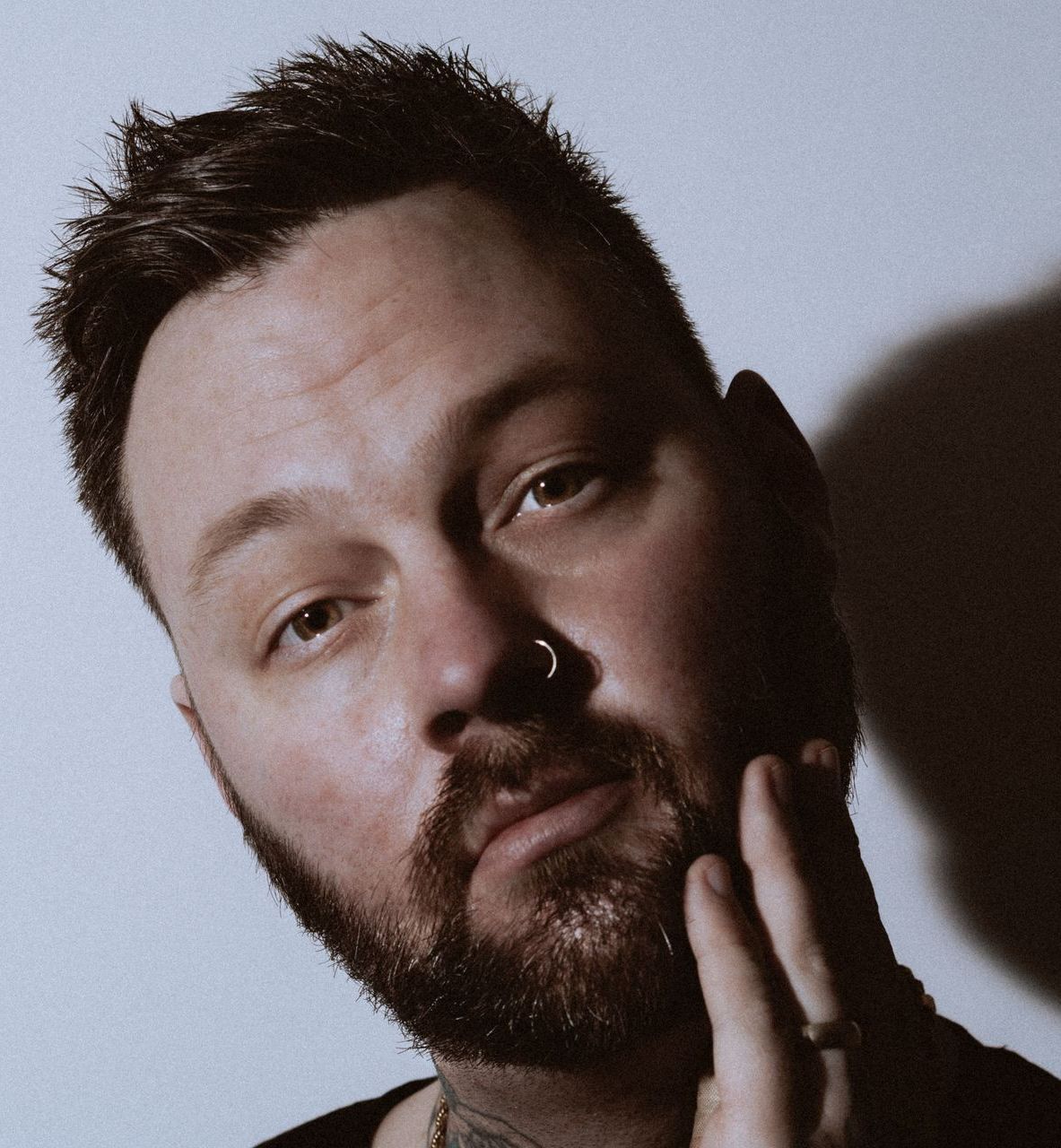 A man with a beard and nose ring is touching his face