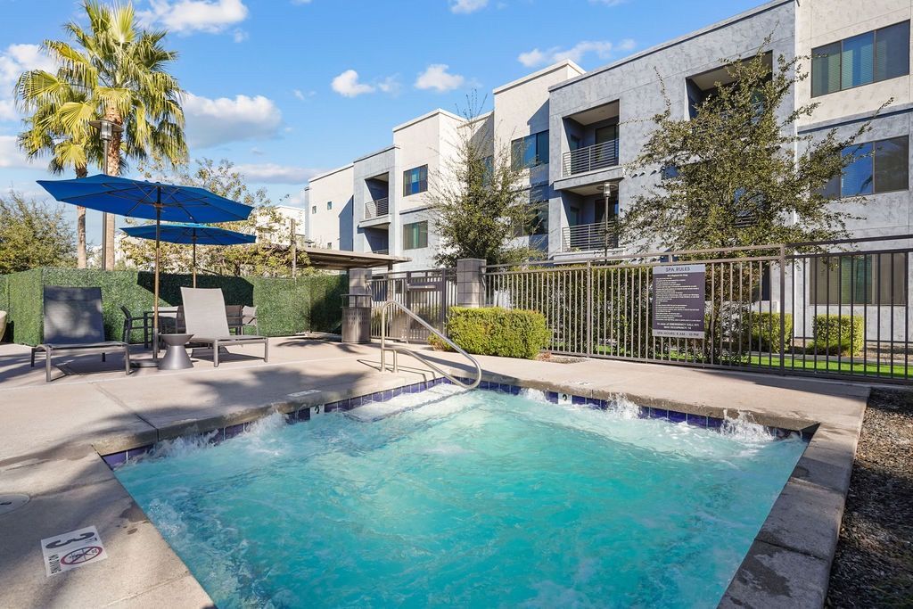 Outdoor swimming pool area with lounge chairs and umbrellas at an apartment complex.