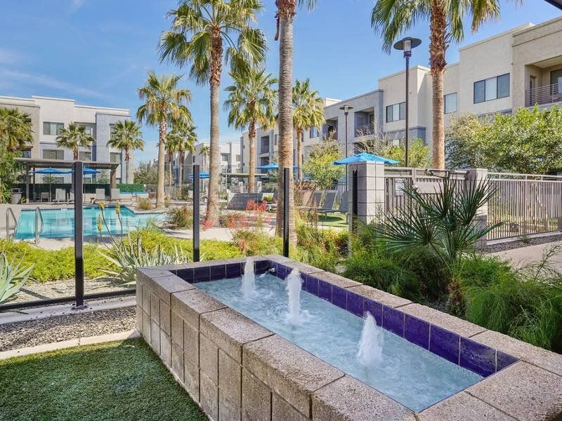 Outdoor pool area with palm trees, fountains, and lounge seating at a multifamily community.