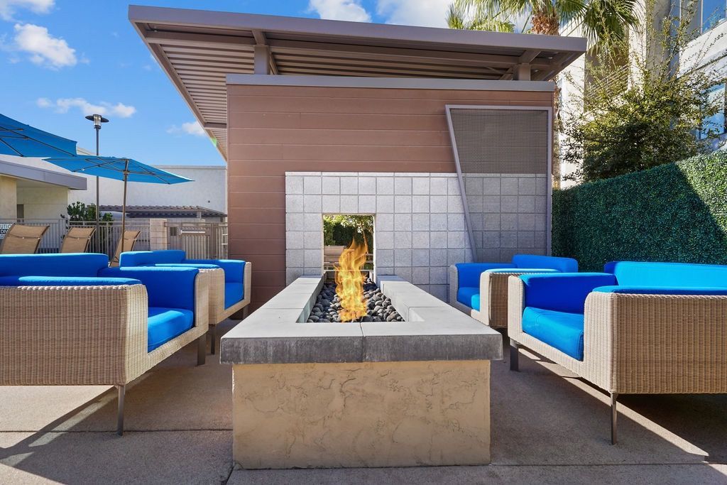 Outdoor community lounge with a rectangular fire pit and blue cushioned chairs.
