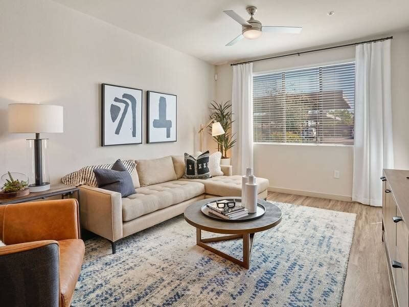Bright apartment living room with beige sofa, round coffee table, and large window.
