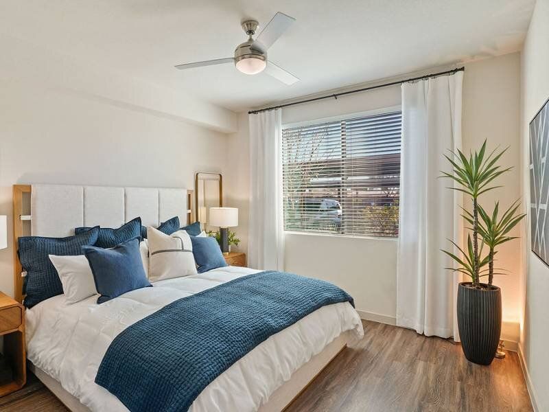 Bright bedroom in a modern apartment with a white upholstered bed and blue bedding.