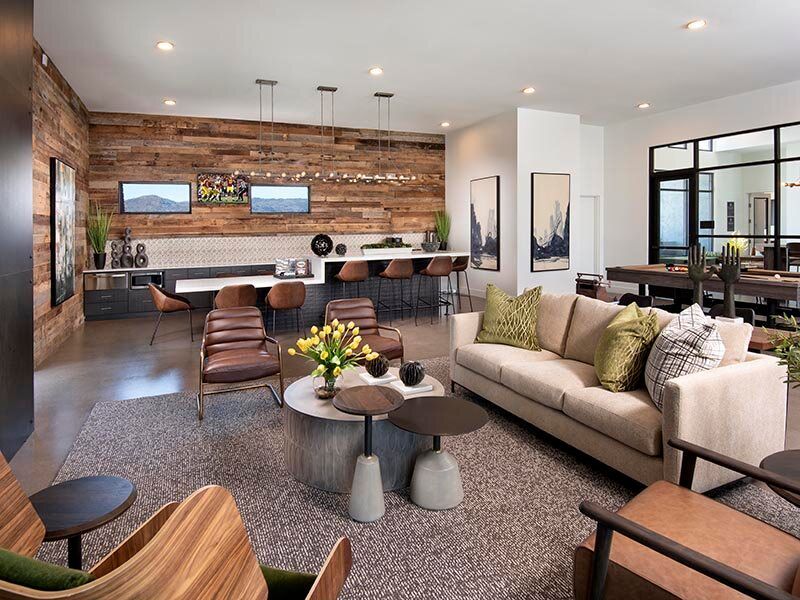 Modern communal lounge with wood accent wall, sofas, chairs, and a bar seating area.