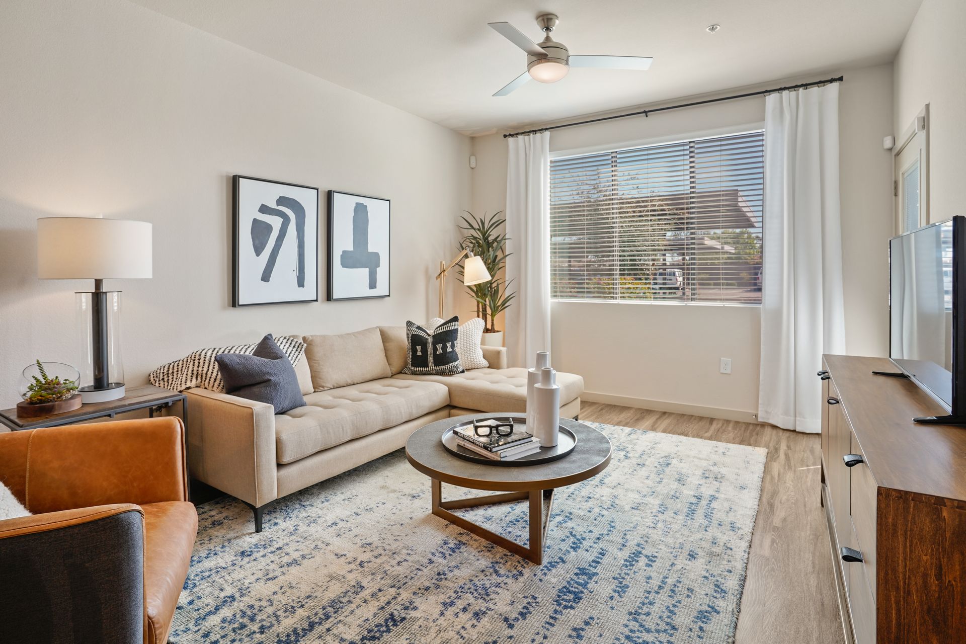 Living room with beige sectional sofa, coffee table, rug, window, and artwork at Parc South Mountain in Phoenix, AZ..