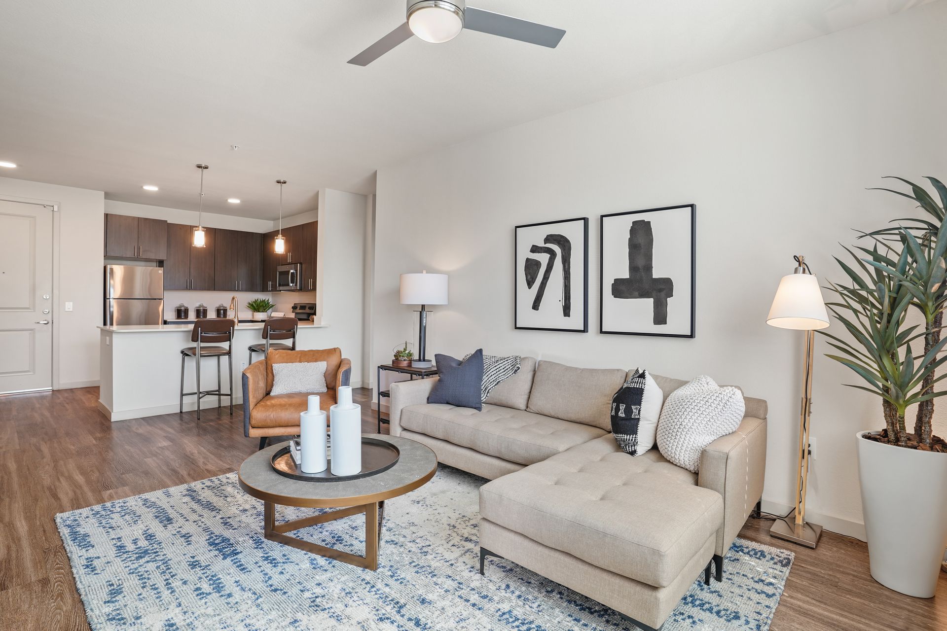 Modern living room with a beige couch, blue rug, and open kitchen at Parc South Mountain in Phoenix, AZ..