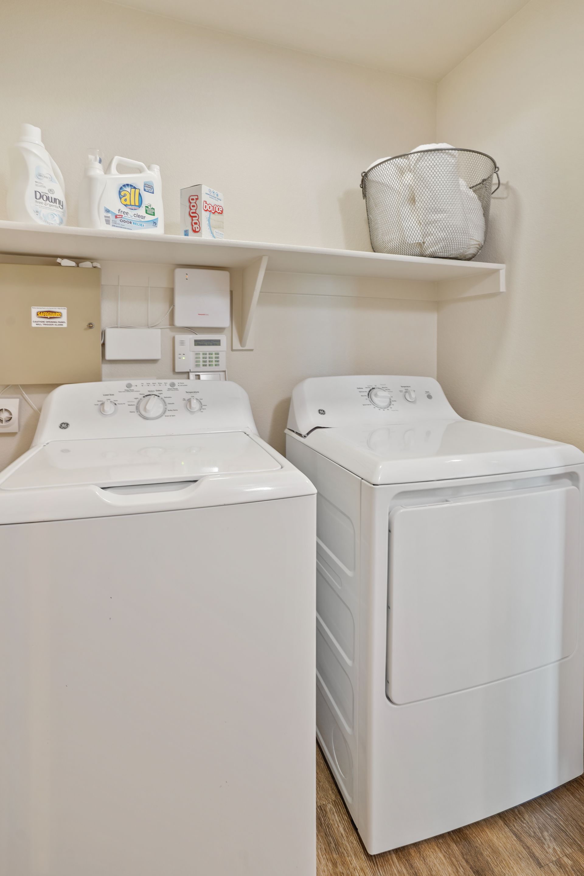 Laundry room with white washer and dryer, shelf with laundry supplies and a basket at Parc South Mountain in Phoenix, AZ..