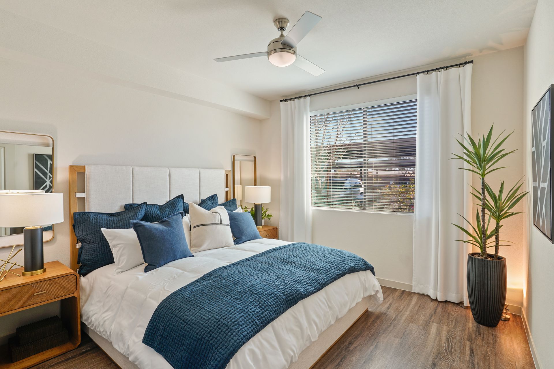 Bedroom with a bed, nightstands, window, and a tall plant. Blue and white decor at Parc South Mountain in Phoenix, AZ..