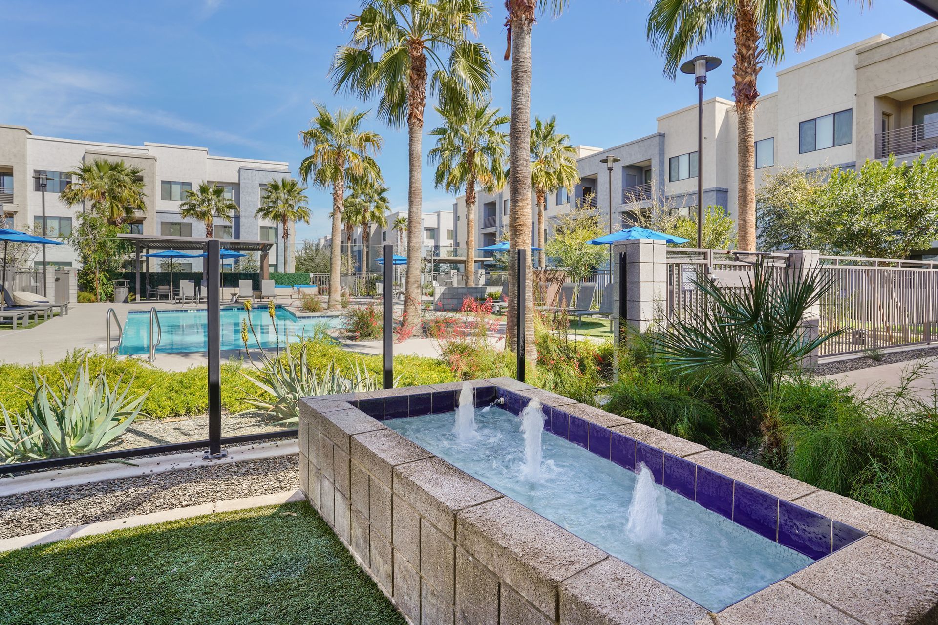 Fountain in a courtyard with a pool, palm trees, and multi-story buildings in the background at Parc South Mountain in Phoenix, AZ..