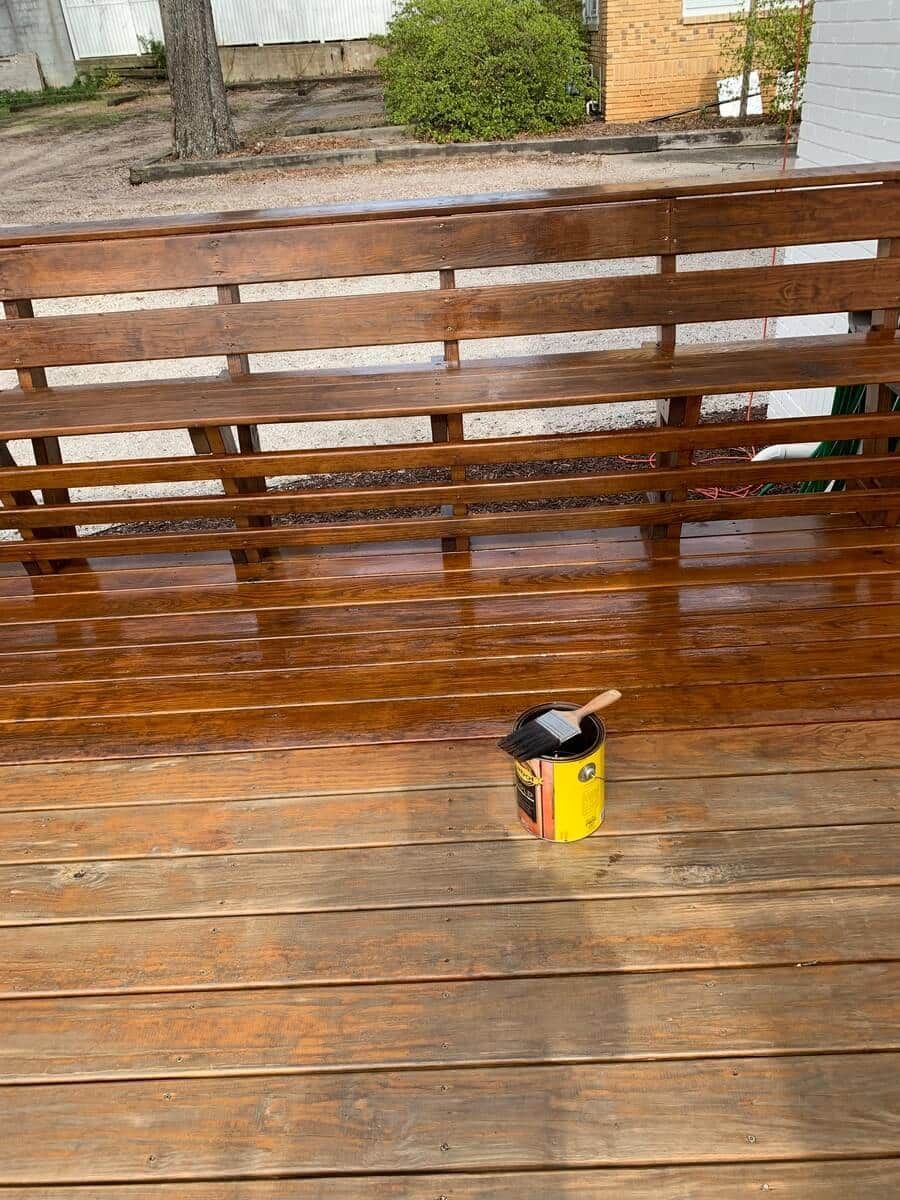 A bucket of paint is sitting on a wooden deck next to a wooden bench.