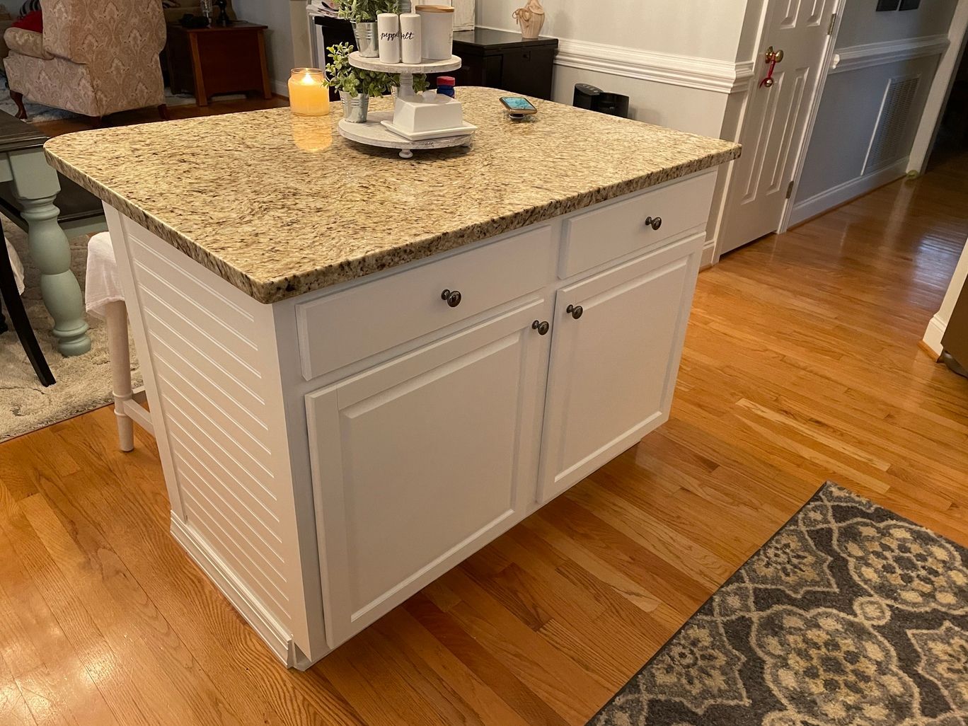 A kitchen island with granite counter tops and white cabinets in a living room.