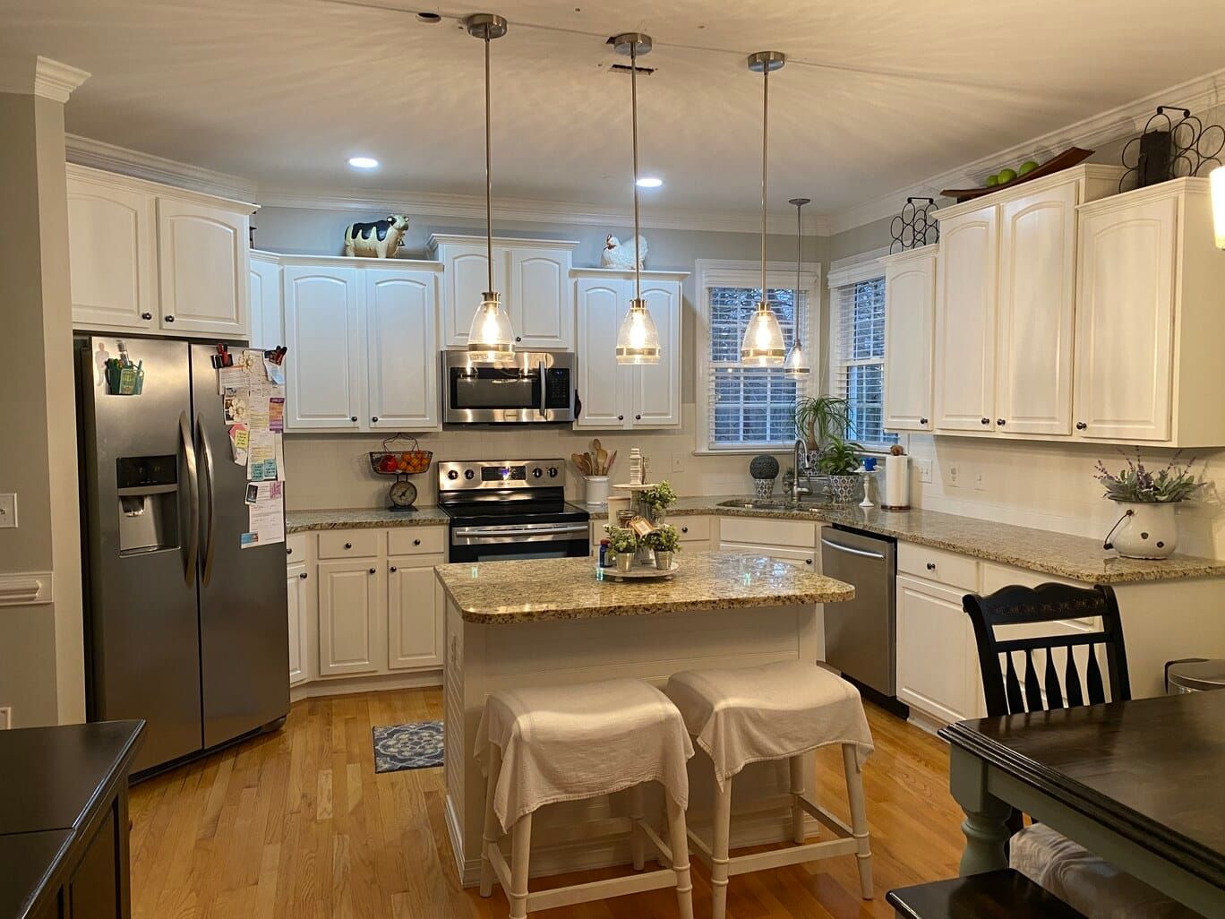 A kitchen with white cabinets , stainless steel appliances , granite counter tops , a table and chairs.