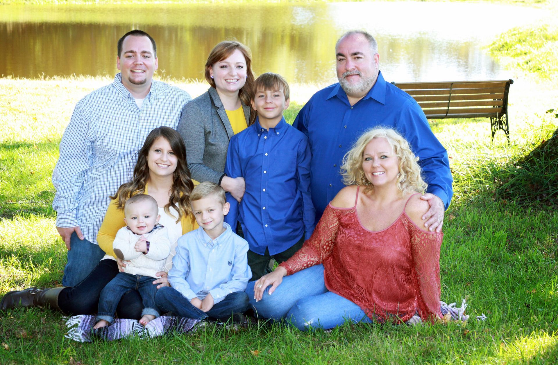 A family is posing for a picture in the grass in front of a lake.