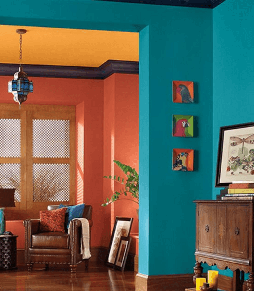 Room with coral, turquoise, and gold walls, brown furniture, and framed art.
