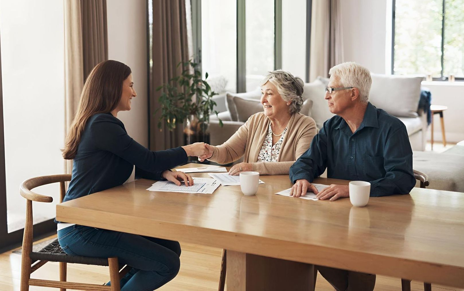 A young woman shakes hands with an elderly woman, while an elderly man sits next to her.