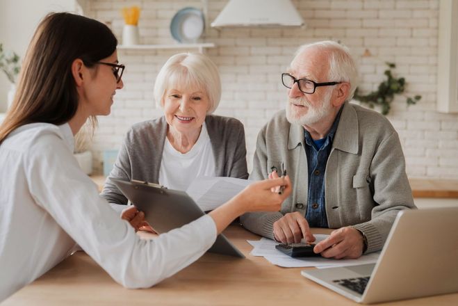 Woman assisting elderly couple with finances at a table, using a laptop and calculator.