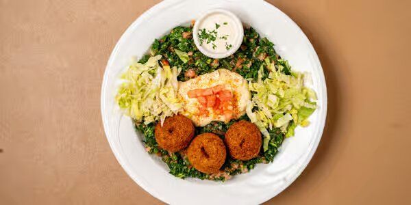 Three falafel patties served with tabouleh salad, hummus, tahini sauce and pita bread.