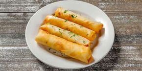 A white plate topped with Cheese rolls on a wooden table.