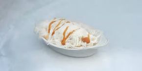 A white bowl filled with ice cream and caramel sauce on a table.