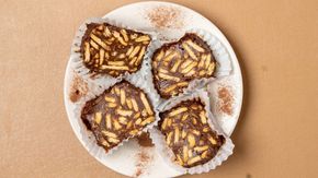 A white plate topped with four brownies covered in chocolate and almonds.