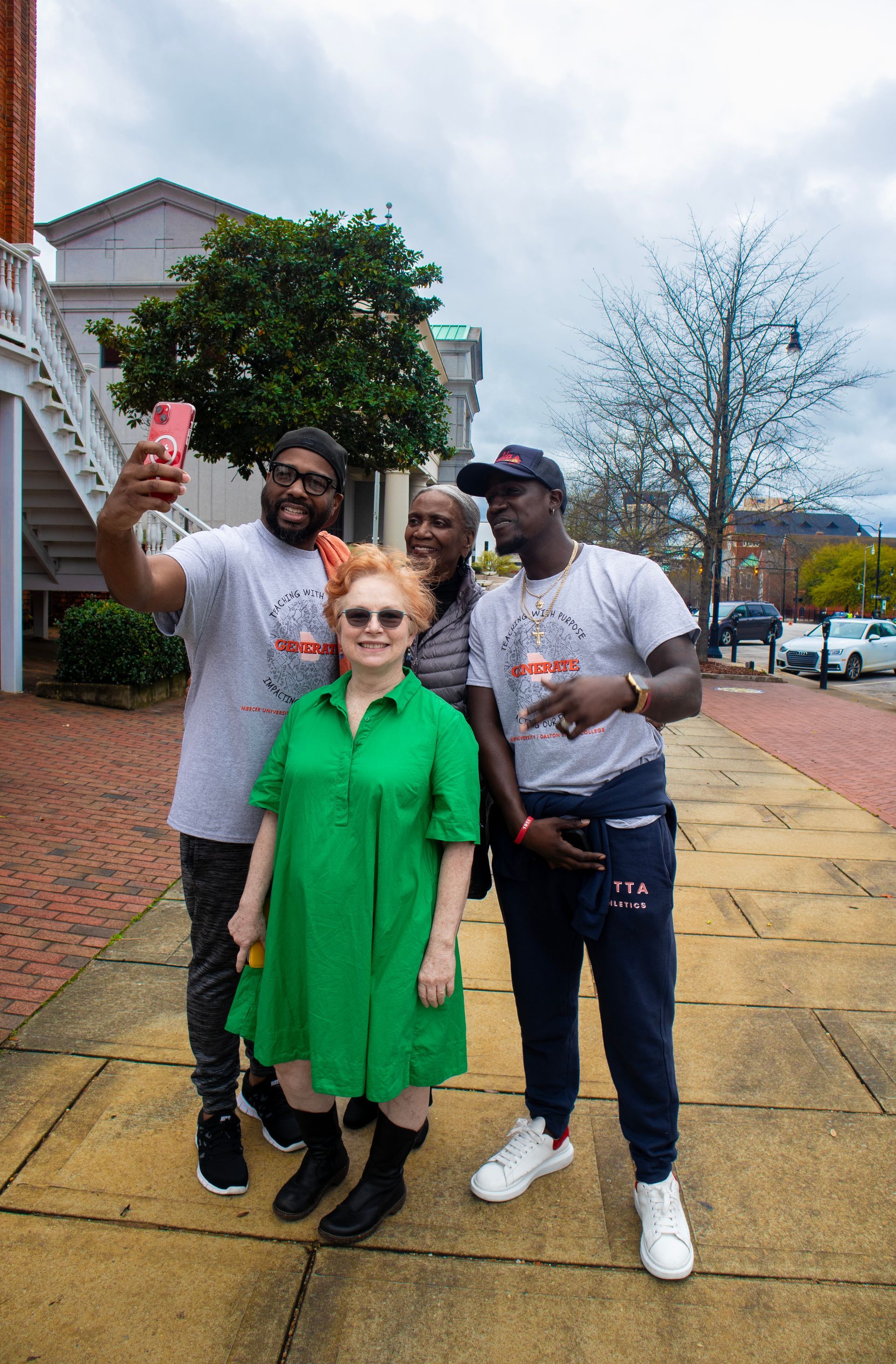 A group of people are standing on a sidewalk taking a selfie.