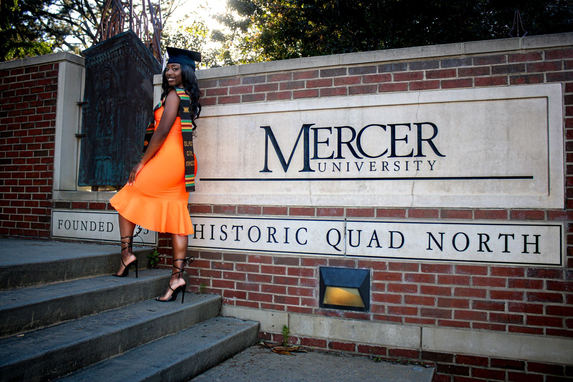 A woman in an orange dress is standing in front of a mercer university sign