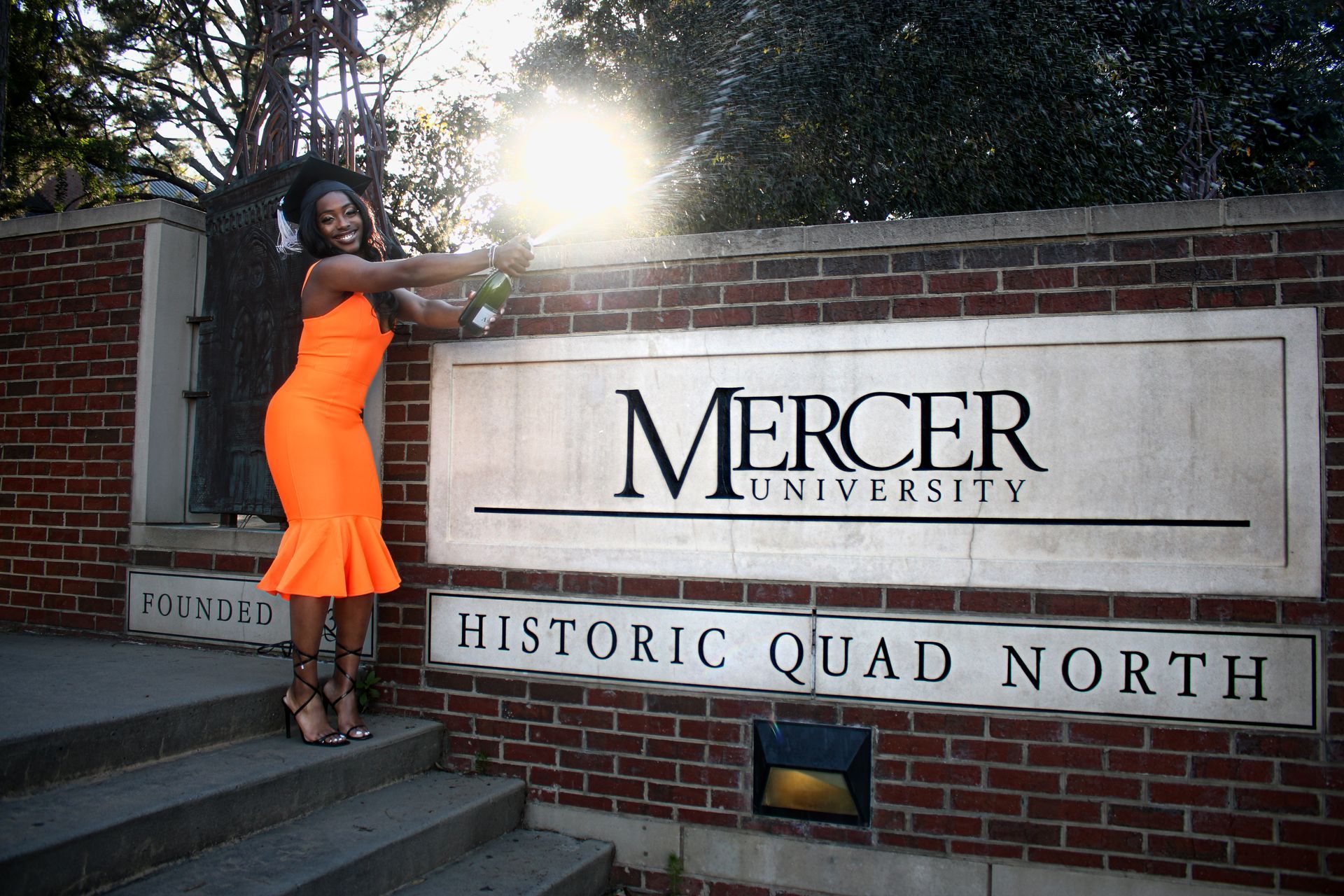 A woman in an orange dress stands in front of a mercer university sign