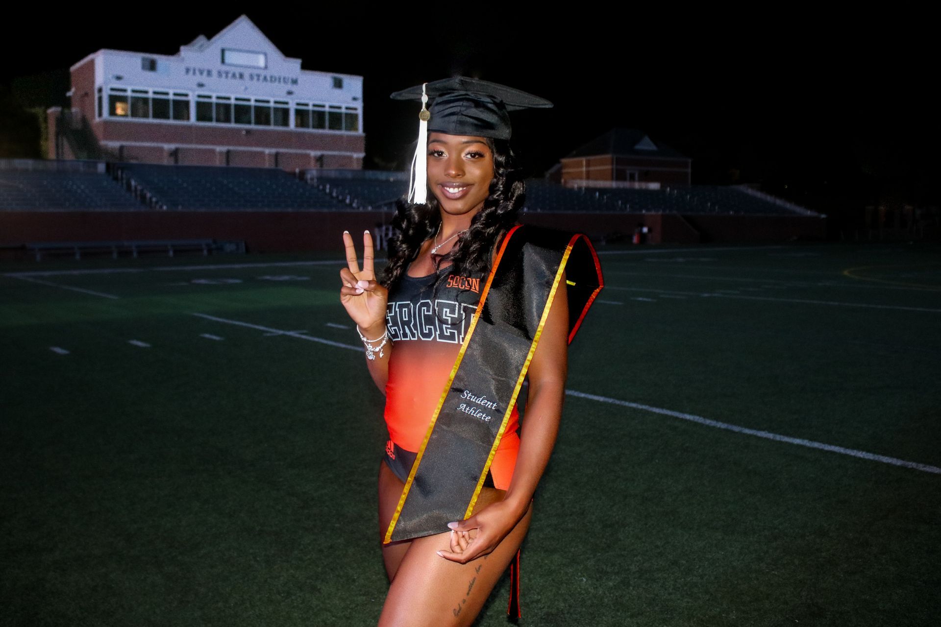 A woman in a graduation cap and gown is standing on a field
